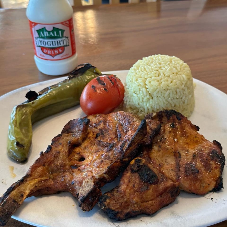 Grilled lamb chops with rice, roasted pepper, tomato, and a bottle of Abali yogurt drink.