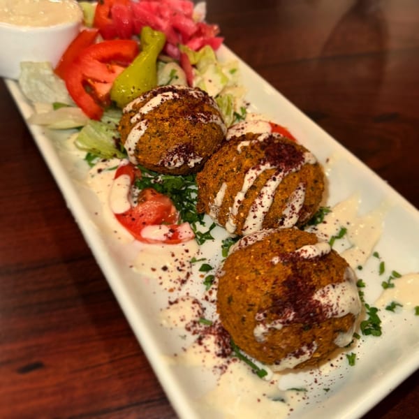 Three falafel balls drizzled with white sauce and sumac, served with salad and pickles.