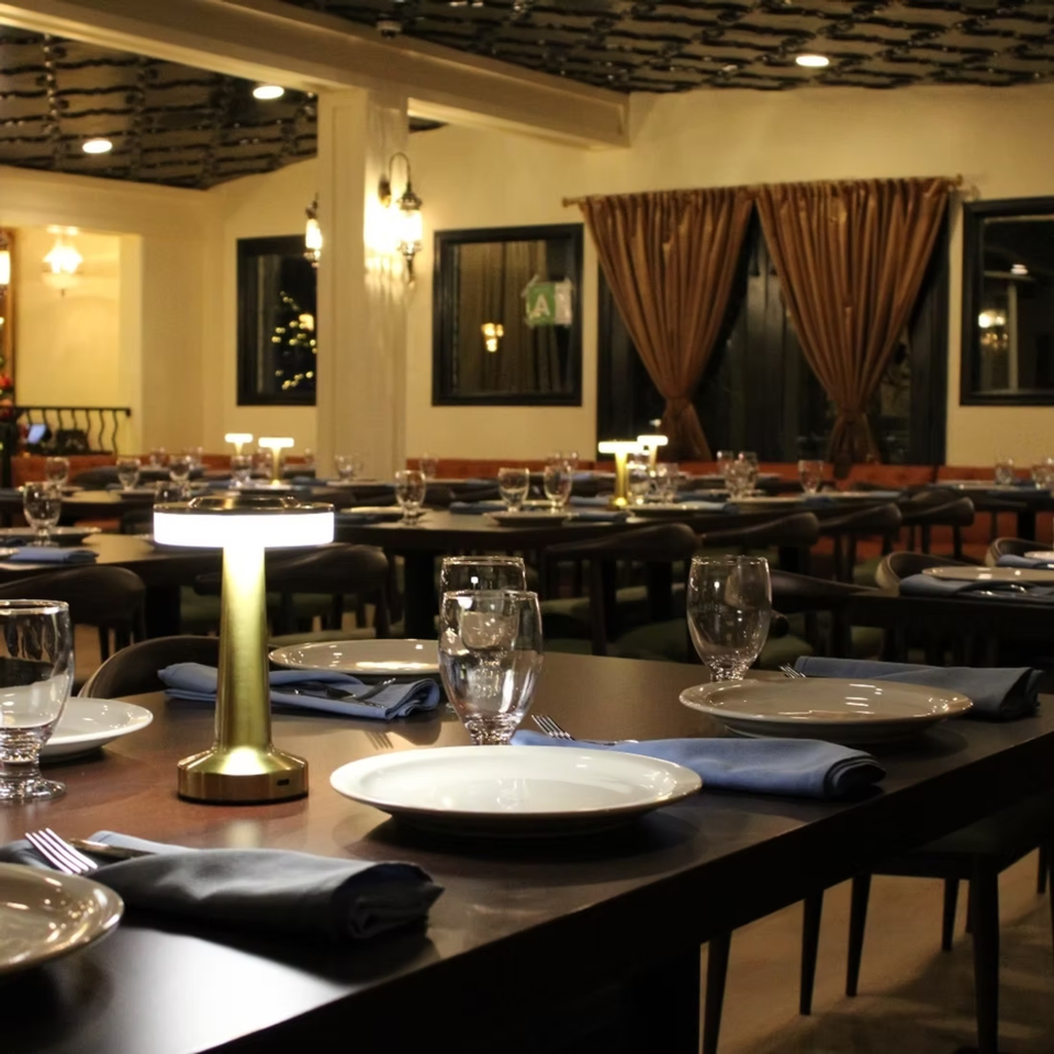 Elegantly set tables with blue napkins and modern lamps in a dimly lit Elena's Greek Armenian Restaurant dining room.