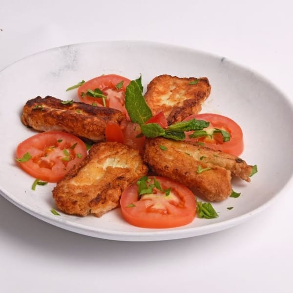 Fried halloumi cheese pieces with sliced tomatoes and fresh herbs on a white plate.