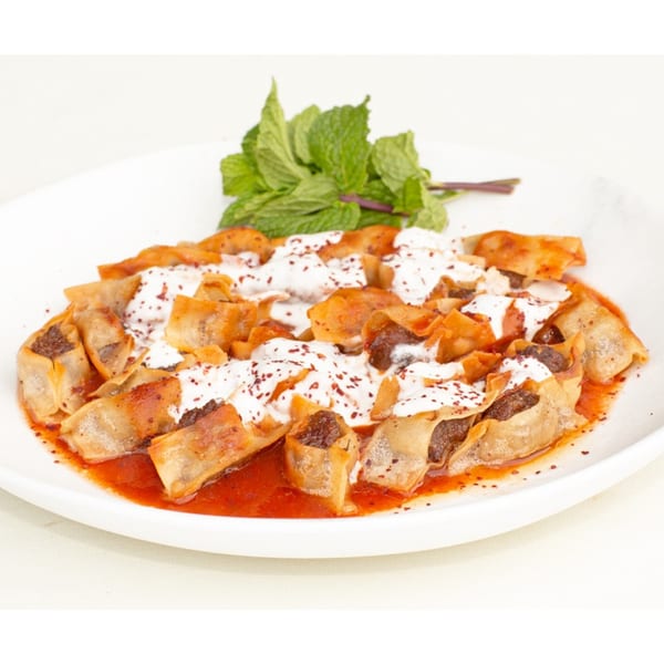 Armenian manti dumplings with yogurt, red sauce, and mint on a white plate.