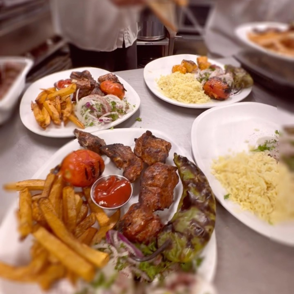 Multiple plates of Elena's Greek Armenian Restaurant's Mediterranean dishes, including kebabs, fries, rice, and grilled vegetables.