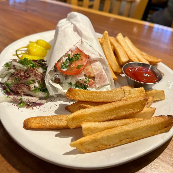 A Mediterranean gyro wrapped in paper, served with french fries, ketchup, and a side salad.