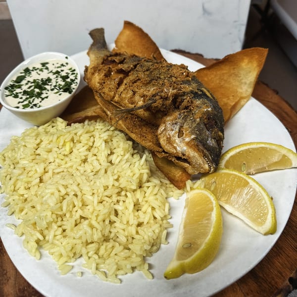 Fried whole fish with rice, lemon wedges, and a side of creamy sauce with herbs.