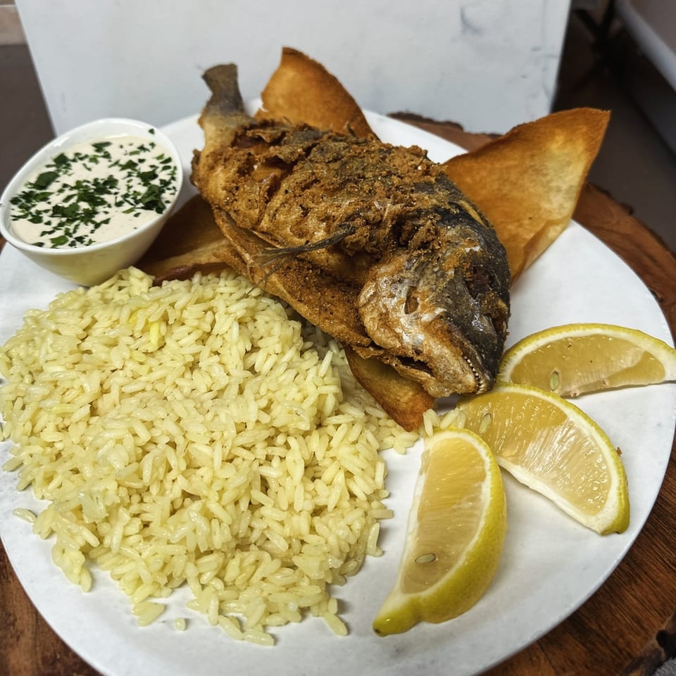 Fried whole fish with rice, lemon wedges, and a side of creamy sauce with herbs.