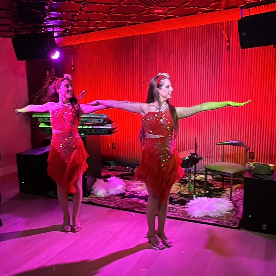 Two women in red sequined dresses performing on a stage with red lighting at Elena's.