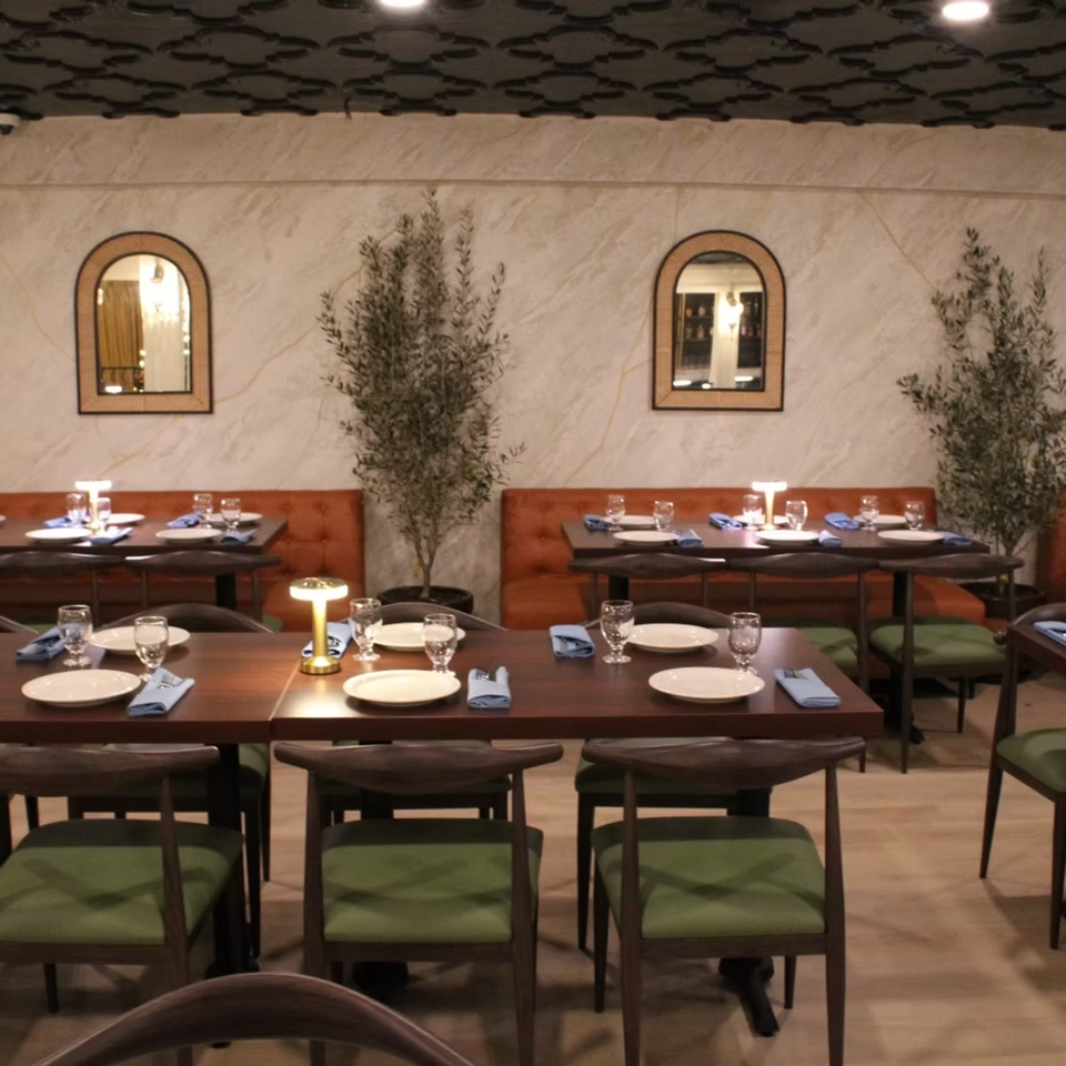 Elena's Greek Armenian Restaurant dining room with set tables, orange booths, and decorative olive trees.