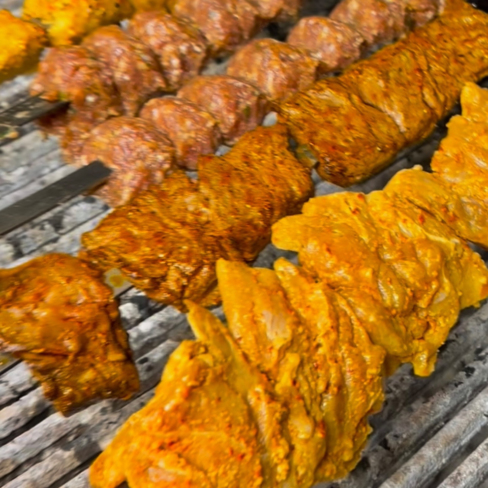 Marinated chicken and beef kebabs grilling on a charcoal barbecue.